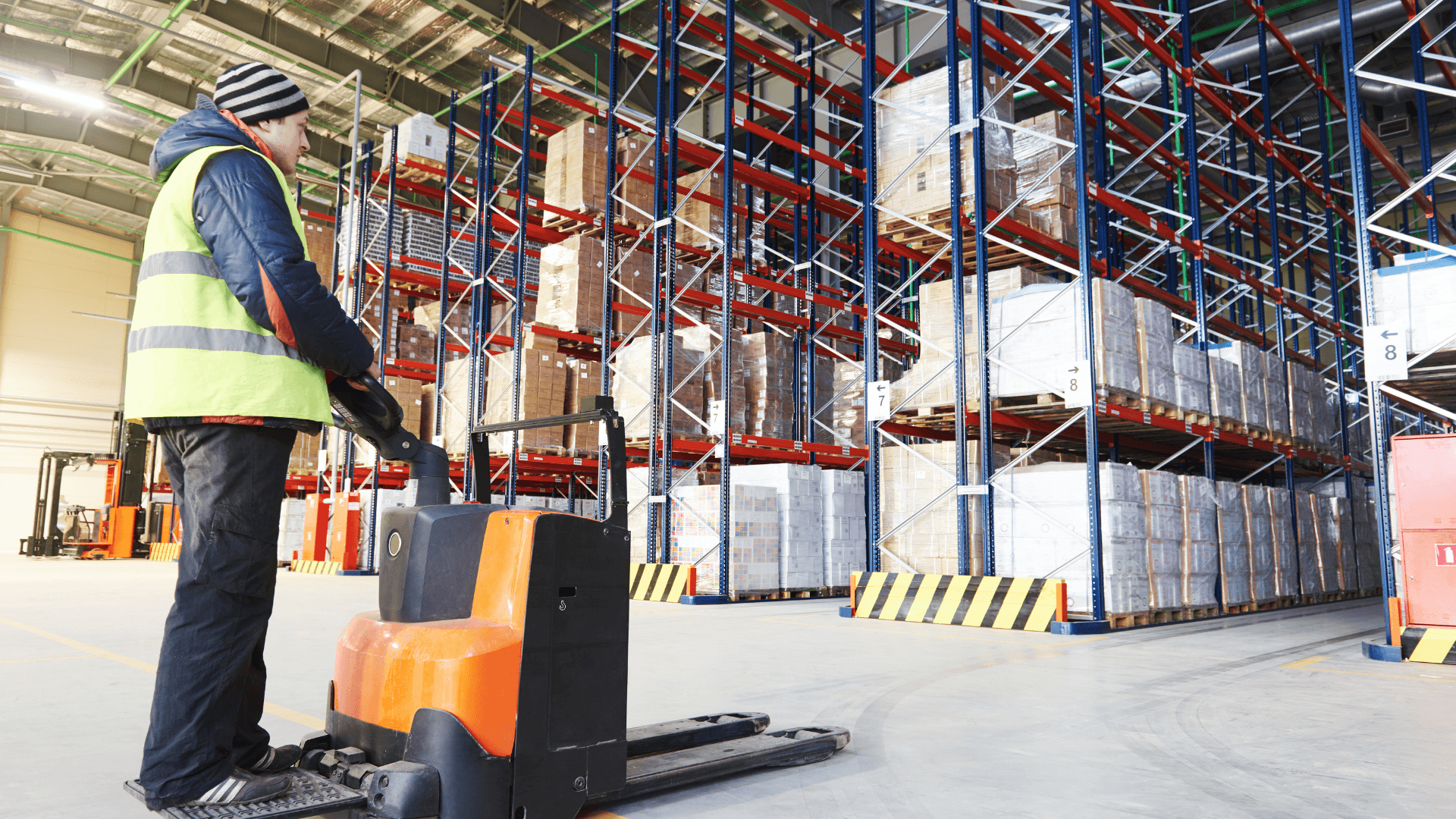 Warehouse operator moving palletized stock through racked storage in Pakistan